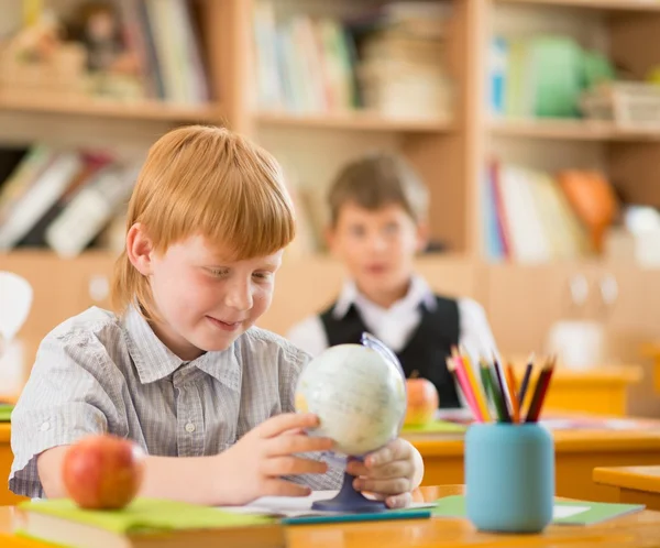 Маленький рыжий школьник позади школьного стола во время урока — стоковое фото