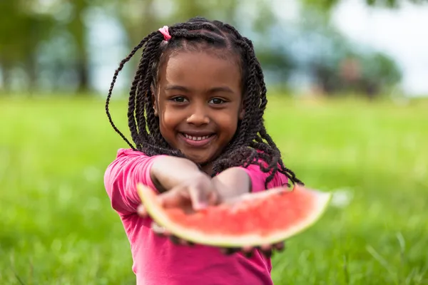 Наружный портрет милой молодой темнокожей маленькой девочки, едящей waterm — стоковое фото