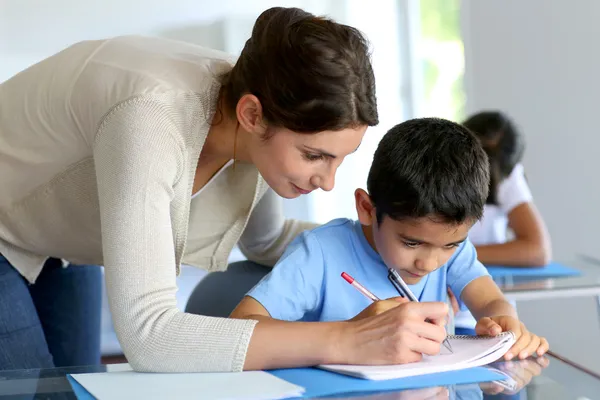 Учитель, помогающий маленькому мальчику с написанием урока — стоковое фото