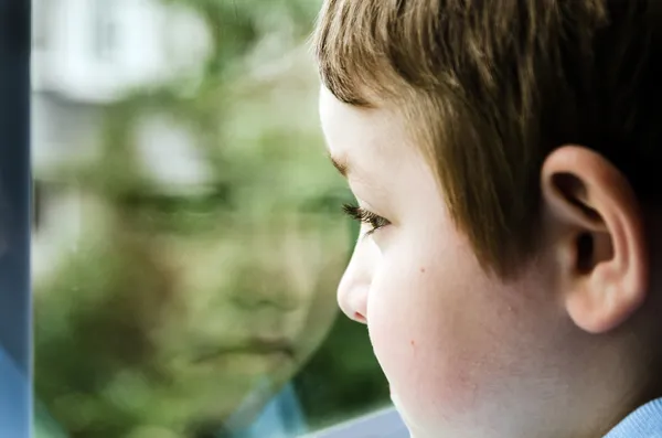 Грустно ребенка, глядя из окна на пасмурный день — стоковое фото