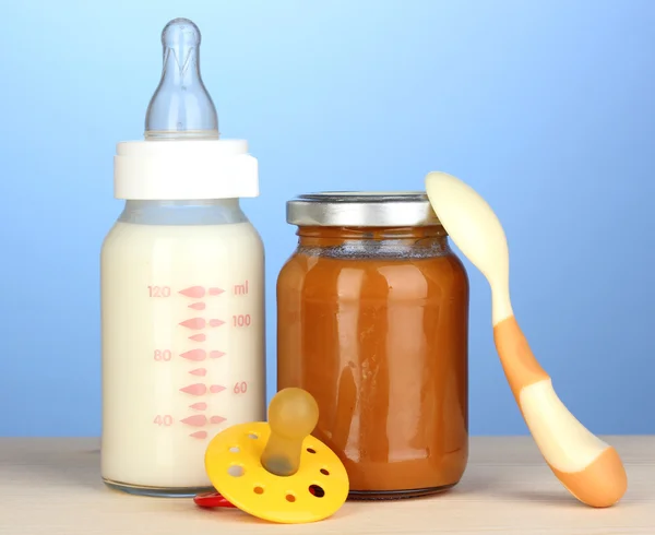 Детское питание, бутылка молока и пюре на синем фоне — стоковое фото