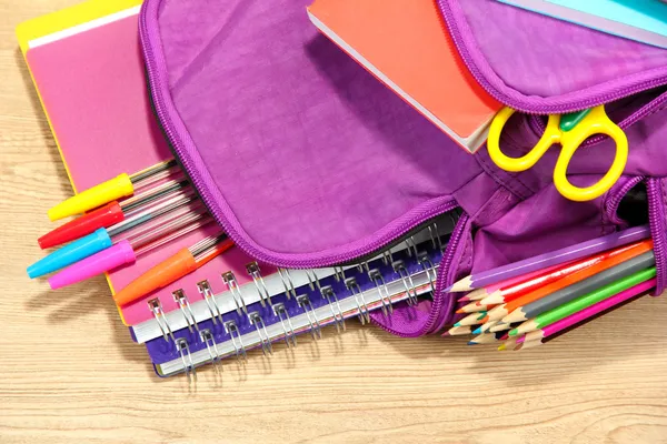 Фиолетовый рюкзак с школой поставляет на деревянных фоне — стоковое фото