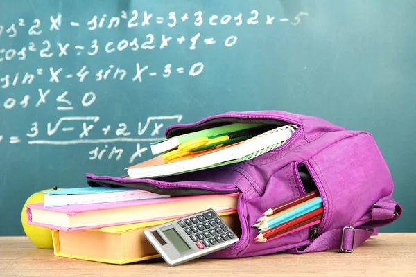 Фиолетовый рюкзак с школой поставляет на деревянный стол на фоне зеленый стол — стоковое фото