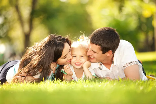 Счастливая мать и отец, целующий их дочь в парк — стоковое фото
