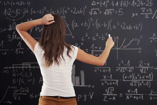 Молодая женщина, глядя на математическую задачу на доске — стоковое фото