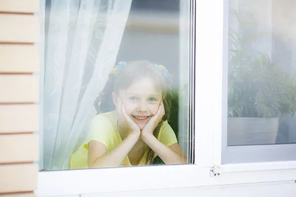 Улыбающаяся девочка смотрит в окно — стоковое фото