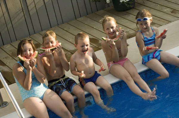 Группа детей, сидя у бассейна, ест арбуз — стоковое фото