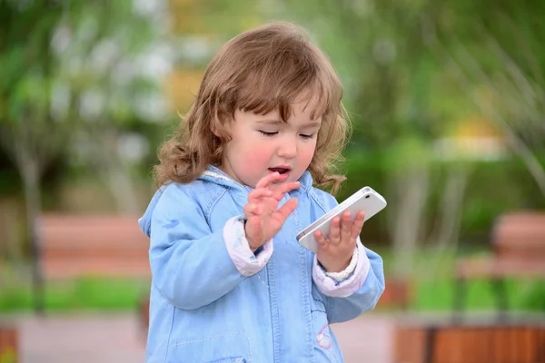 Девушка два года, с мобильного телефона в парке — стоковое фото