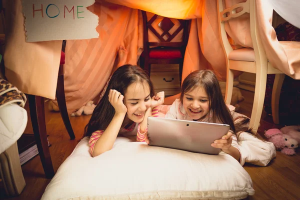 Счастливые девушки с помощью цифрового планшета в доме из одеяла — стоковое фото