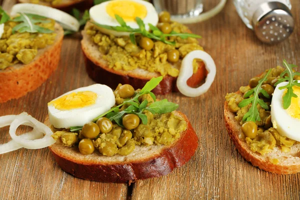 Сэндвичи с зеленой пастой гороха и вареное яйцо с луковыми кольцами и лимоном на деревянном фоне досок — стоковое фото