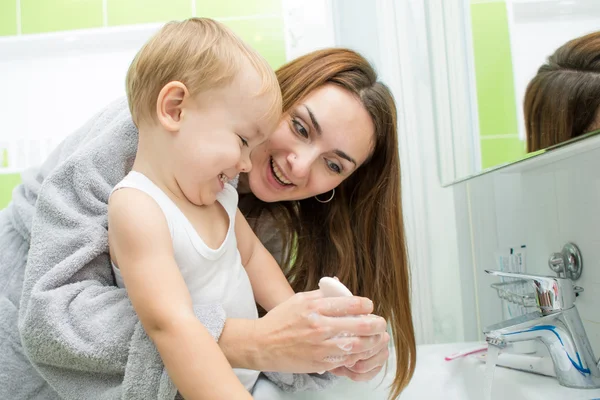 Счастливая мать и ребенок, моющий руки с мылом в ванной — стоковое фото