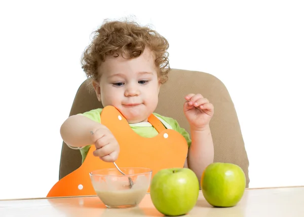 Маленький ребенок ест ложкой, сидя за столом с фруктами — стоковое фото