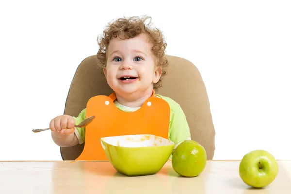 Маленький ребенок ест ложкой, сидя за столом с фруктами — стоковое фото