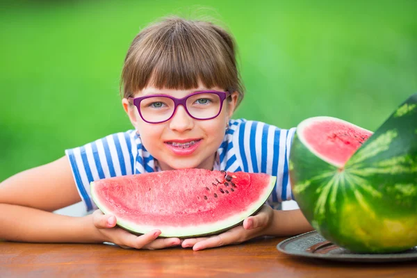 Child eating watermelon. Kids eat fruits in the garden. Pre teen girl in the garden holding a slice of water melon. happy girl kid eating watermelon. Girl kid with gasses and teeth braces — стоковое фото