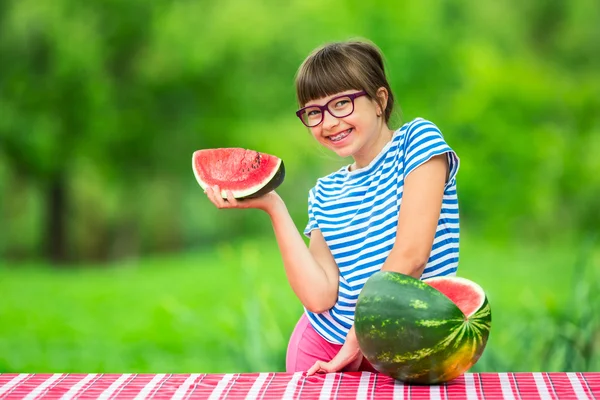 Child eating watermelon. Kids eat fruits in the garden. Pre teen girl in the garden holding a slice of water melon. happy girl kid eating watermelon. Girl kid with gasses and teeth braces — стоковое фото