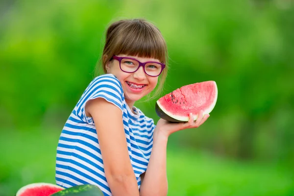 Child eating watermelon. Kids eat fruits in the garden. Pre teen girl in the garden holding a slice of water melon. happy girl kid eating watermelon. Girl kid with gasses and teeth braces — стоковое фото