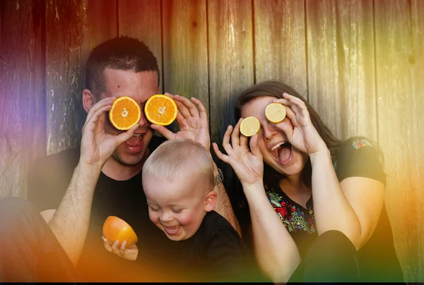 Семья с маленьким мальчиком, весело проводящим время с апельсинами — стоковое фото