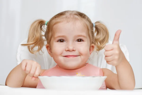 Счастливый маленькая девочка ест ложкой сидя за столом — стоковое фото
