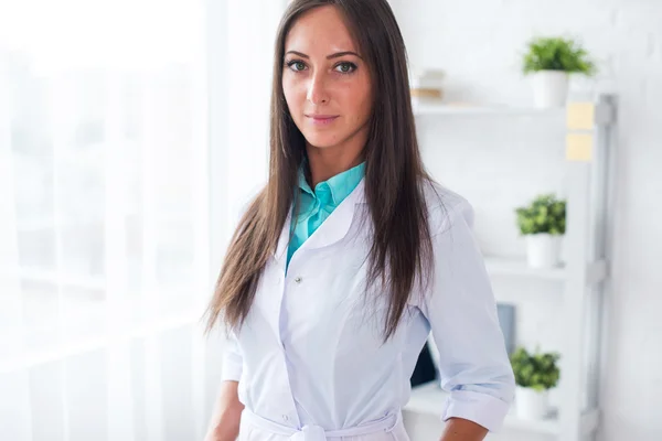 Портрет молодой женщины врач с белым пальто стоял в медицинском кабинете, глядя на камеру — стоковое фото