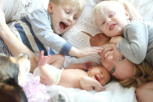 Счастливая молодая мать и трое детей, прижимаясь на кровати — стоковое фото