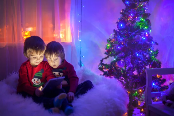Два мальчика, играющие на таблетке дома, следующий за рождественской елкой — стоковое фото