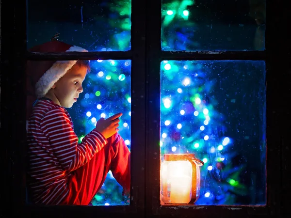 Милый мальчик, сидя на окно щит, играя на мобильный телефон на — стоковое фото