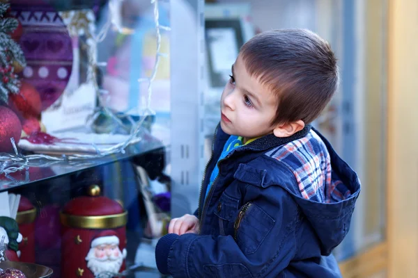 Сладкий маленький мальчик, глядя через окно в магазин, украшенные fo — стоковое фото