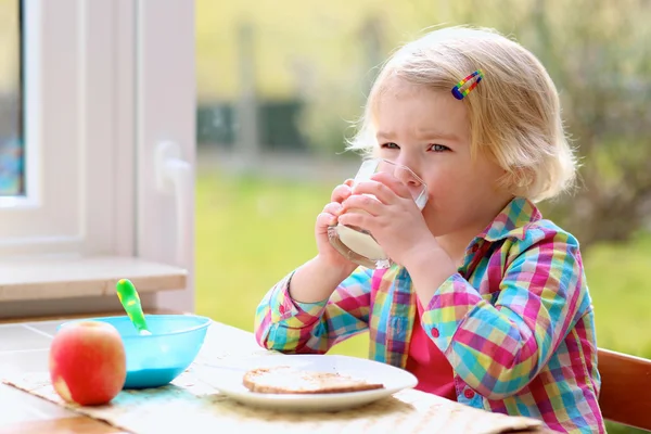 Маленькая девочка, имеющая тост и молоко на завтрак — стоковое фото