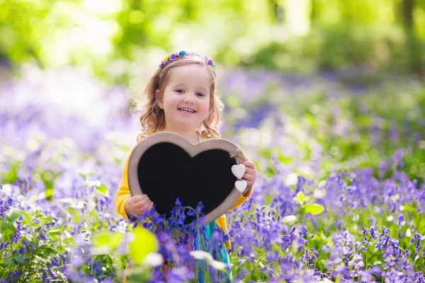 Little girl with blank board in flower field — стоковое фото