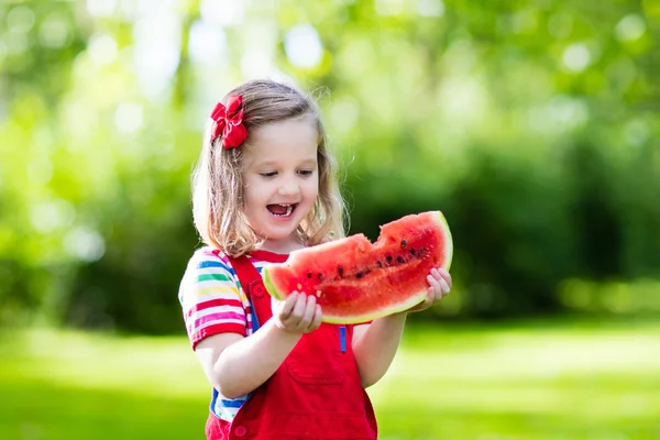 Маленькая девочка ест арбуз в саду — стоковое фото