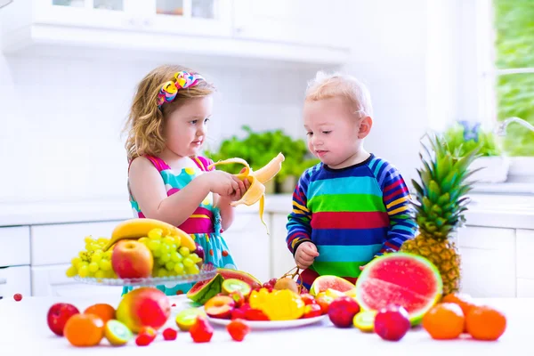 Дети, едящие фрукты в белой кухне — стоковое фото