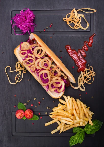 Хот-дог с кольцами лука, капуста, помидоры и картофель на доске темный — стоковое фото