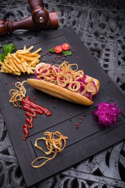 Хот-дог с кольцами лука, капуста, помидоры и картофель на доске темный — стоковое фото