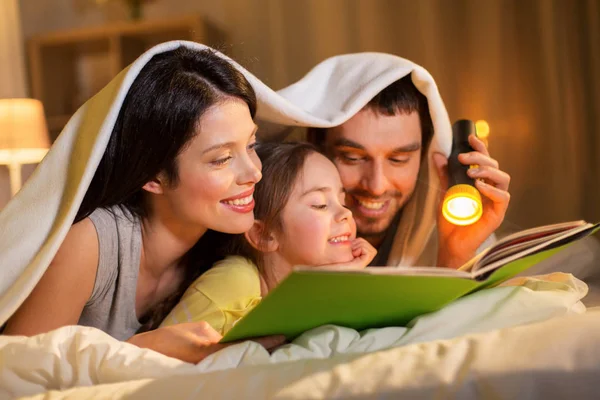Счастливые семьи чтения книги в постели ночью у себя дома — стоковое фото