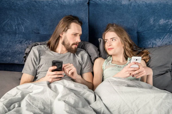 Пара в постели со смартфонами — стоковое фото