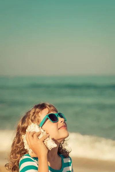 Счастливый ребенок слушать раковины на пляже — стоковое фото