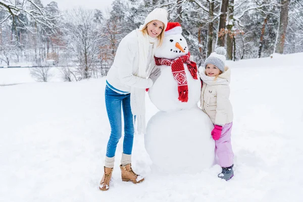 Красивые Счастливая Мать Дочь Улыбаясь Камеру Стоя Снеговика Зимнем Парке — стоковое фото