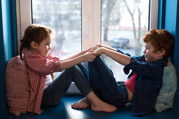 Очаровательны Мало Дети Взявшись Руки Улыбаются Друг Другу Сидя Подоконнике — стоковое фото