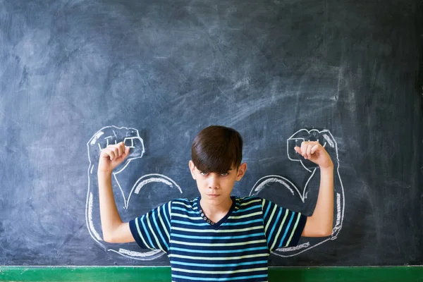 Сильный ребенок мужского пола, показывая мышцы в классе на уроке — стоковое фото