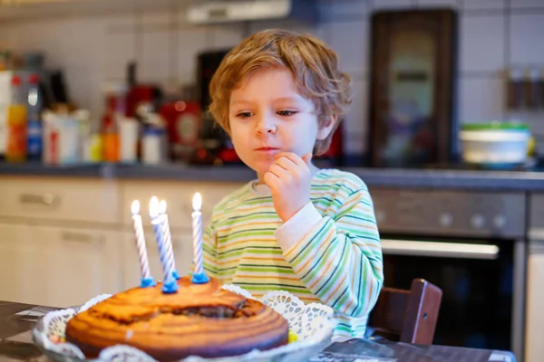 Маленький малыш мальчик празднует свой день рождения и дует свечи на торт — стоковое фото
