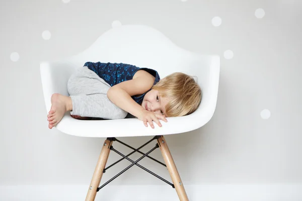 Счастливое беззаботное детство. Сладкий Кавказский младенца прокатки себя в белый дизайнер стул, скрываясь от своих друзей во время игры в прятки. Милый ребенок мальчик весело в помещении. Визуальные эффекты — стоковое фото