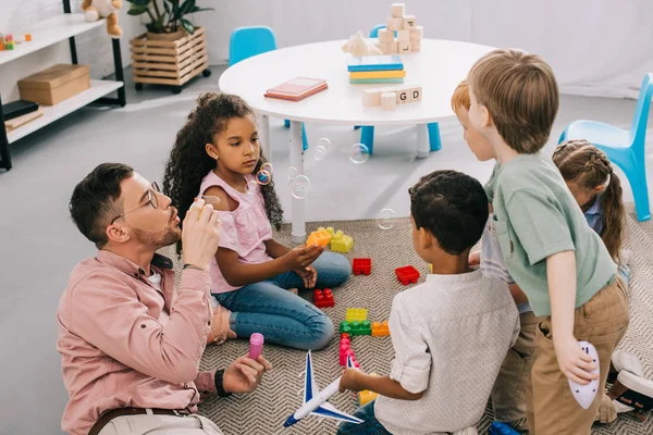 Teacher Soap Bubbles Multicultural Preschoolers Sitting Floor Colorful Bricks Classroom — стоковое фото