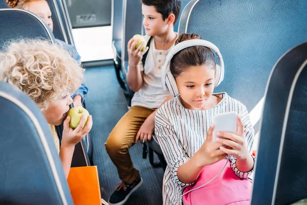 Adorable Little Schoolgirl Using Smartphone Listening Music Headphones While Riding — стоковое фото