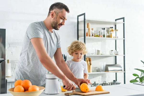 Man Cutting Orange Knife Making Fresh Juice While His Son — стоковое фото