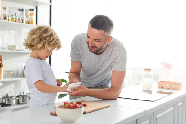 Smiling Father Helping Son Wiping Hands Napkin Tabletop Strawberries Kitchen — стоковое фото