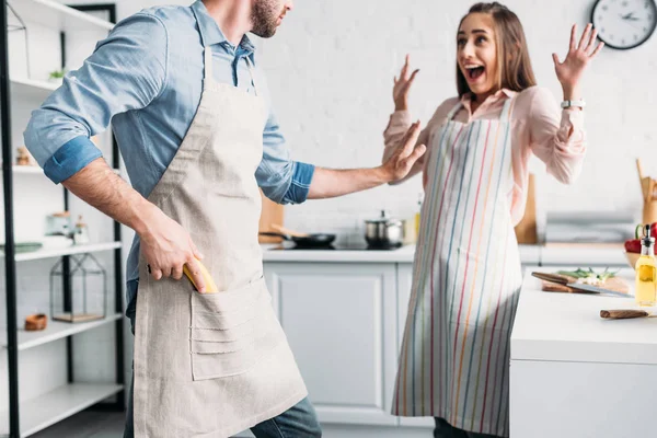 Excited Girlfriend Standing Hands Boyfriend Holding Banana Gun Kitchen — стоковое фото