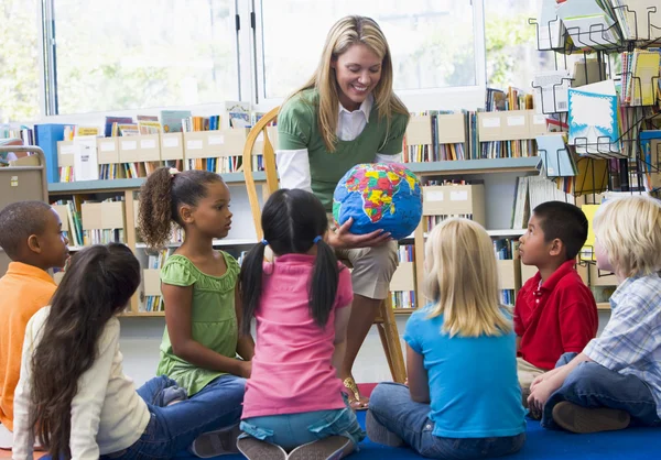 Воспитателя и детей, глядя на глобус в библиотеке — стоковое фото