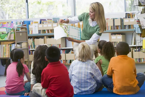 Воспитатель детского сада, читающий детям в библиотеке — стоковое фото
