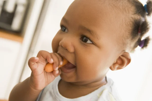 Молодая девочка ест морковь в помещении — стоковое фото
