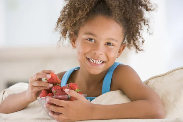 Молодая девочка ест клубнику в гостиной улыбается — стоковое фото